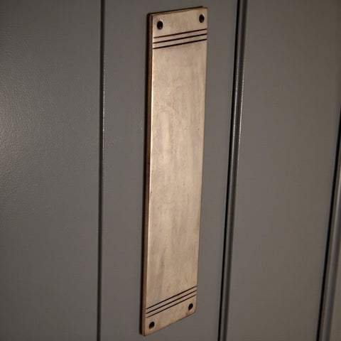 Unlacquered antique reeded push plate fitted to painted door, showing vertical installation and naturally aged surface