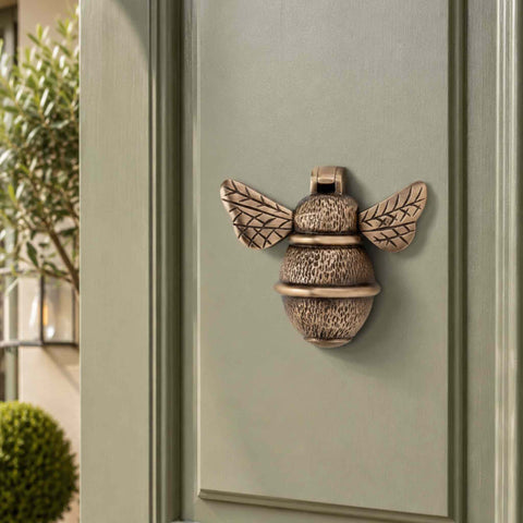 Antique brass bumble bee door knocker fitted to a sage green front door with traditional panelling