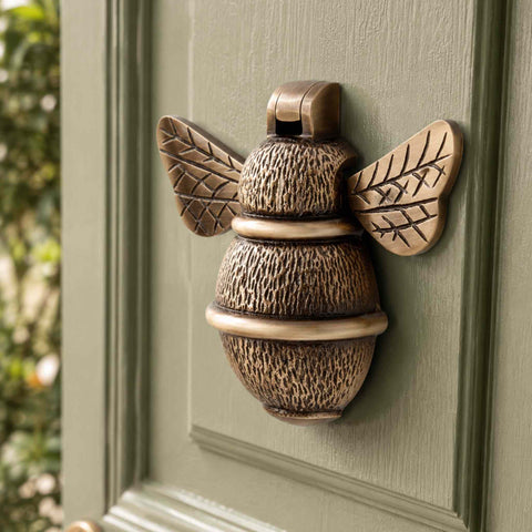 Antique brass bumble bee door knocker mounted on a sage green entrance door showing textured detailing
