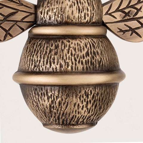 Detailed view of antique brass bumble bee door knocker highlighting textured cast body