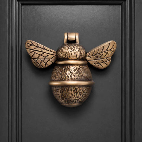 Antique brass bumble bee door knocker mounted on a black panelled front door