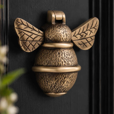 Close-up of antique brass bumble bee door knocker showing detailed textured body and engraved wings