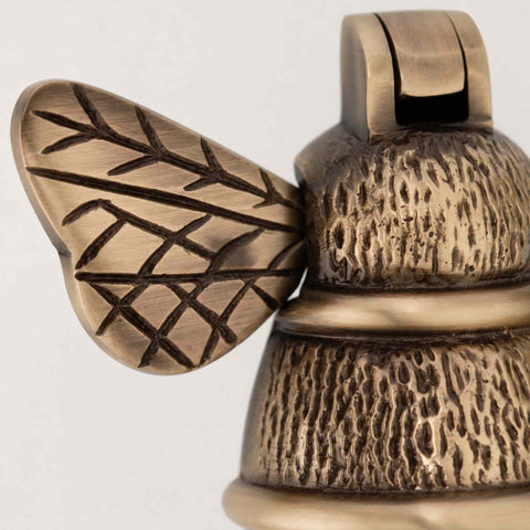 Detailed macro shot of antique brass bumble bee door knocker wing showing engraved decorative detailing