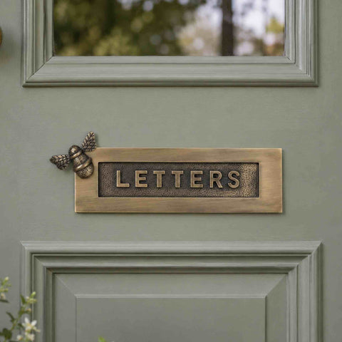 Antique brass bumble bee "LETTERS" letter plate installed on a sage green entrance door with decorative bee detail and raised lettering.