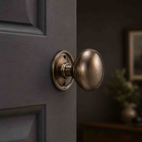 Antique brass cottage door knob with round backplate fitted to a dark grey panelled internal door.
