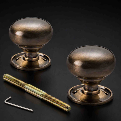 Antique brass cottage door knob pair with round backplates, threaded spindle and Allen key on a dark background.