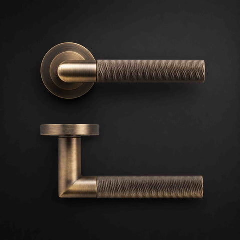 Antique brass knurled lever door handle pair shown from front and side on a dark background, highlighting the textured grip and round rose.