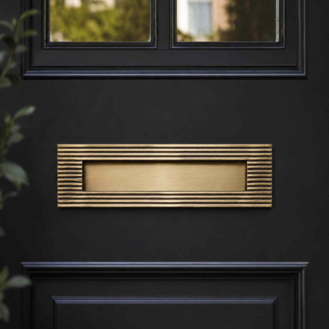 Antique brass reeded solid brass letter box plate mounted on a black front door