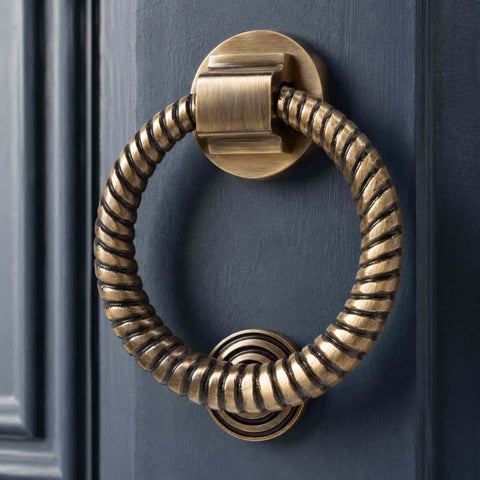 Antique brass reeded ring door knocker installed on a dark blue front door