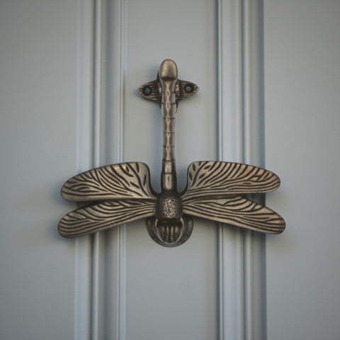 Antique dragonfly door knocker mounted on a panelled grey front door