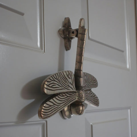 Antique dragonfly door knocker fitted to a grey door.