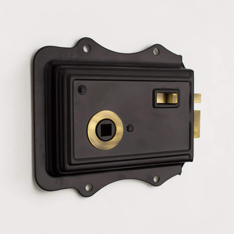 Front view of black Victorian style rim lock with antique brass latch detail and decorative fixing plate.