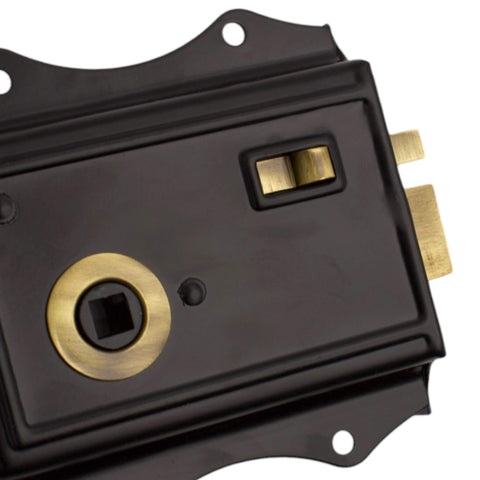 Close-up detail of black and antique brass rim lock showing latch release and spindle opening.
