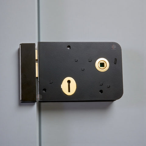 Black and polished brass Scotch rim lock fitted to painted timber door showing traditional surface-mounted design