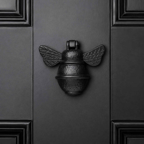 Black cast iron bumble bee door knocker centred on a black panelled front door