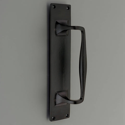 Black cast iron door pull handle mounted vertically on a door, fixed to a rectangular backplate.