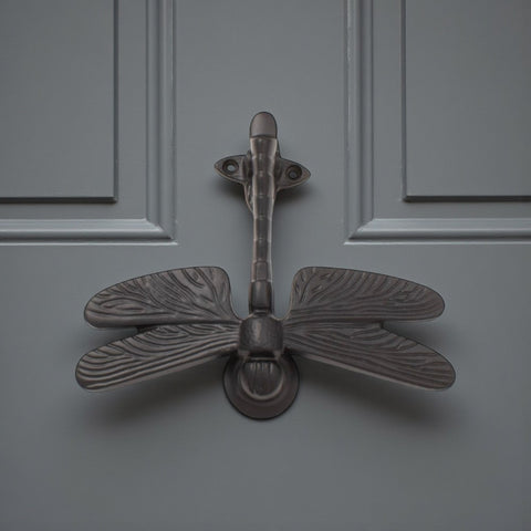 Black cast iron dragonfly door knocker fitted to a grey door.