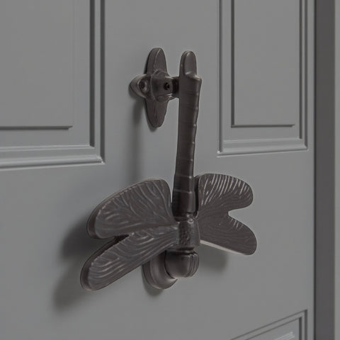 Angled view of black cast iron dragonfly door knocker on grey door.