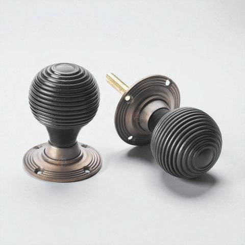 Pair of black ebonised beehive door knobs with matt antique backplates displayed on a light grey background.