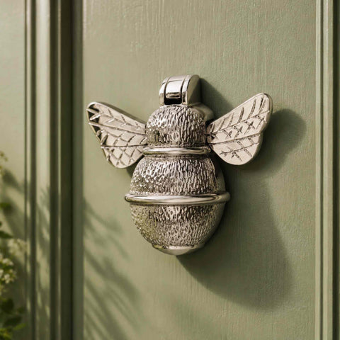 Polished nickel bumble bee door knocker fitted to a sage green front door with decorative panelling