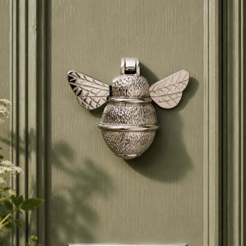 Polished nickel bumble bee door knocker mounted on a sage green entrance door showing textured body detailing