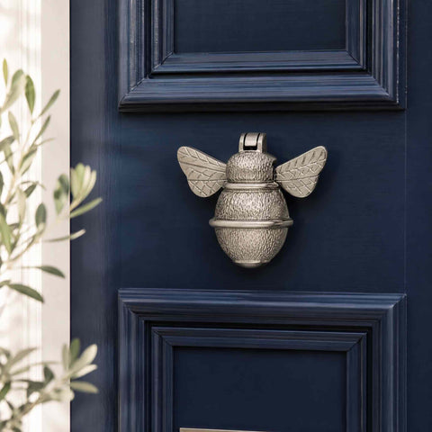 Polished nickel bumble bee door knocker mounted on a navy blue panelled front door
