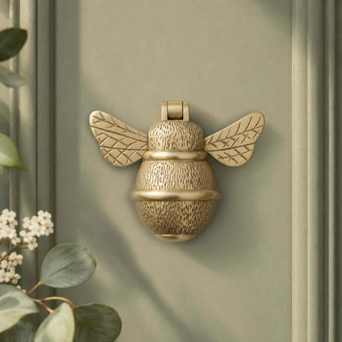 Satin Brass Bumble Bee Door Knocker fitted to a sage green front door with decorative foliage and soft natural lighting.
