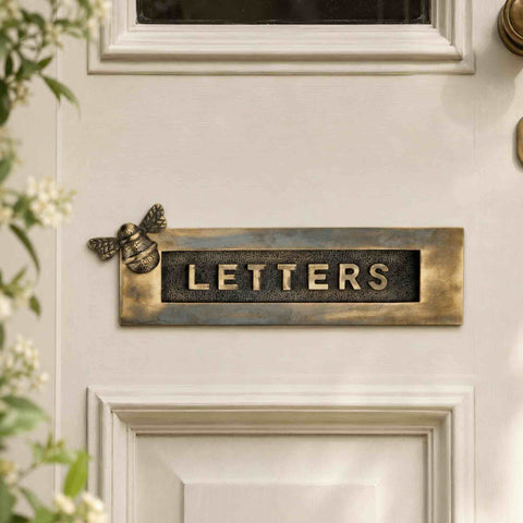 Unlacquered aged brass bumble bee "LETTERS" letter plate fitted to a cream front door, featuring an authentic aged brass patina, decorative bee detail and traditional raised lettering.