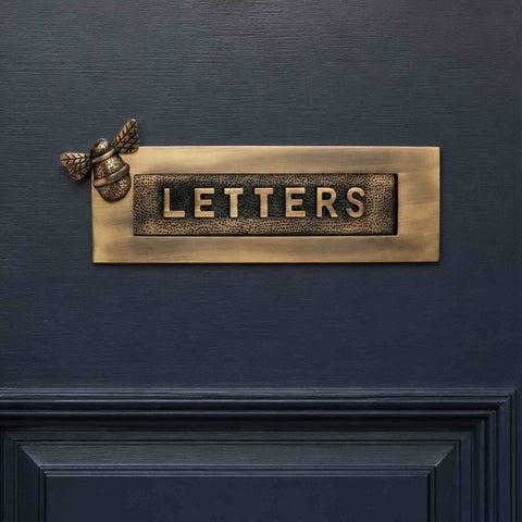 Antique brass bumble bee "LETTERS" letter plate mounted on a dark blue front door, featuring a decorative bee detail and traditional raised lettering.