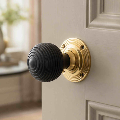 Ebonised black beehive rim mortice door knob with an unlacquered polished brass backplate installed on a painted interior door.