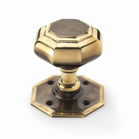 Close-up of a large aged brass octagonal mortice door knob with matching octagonal backplate.