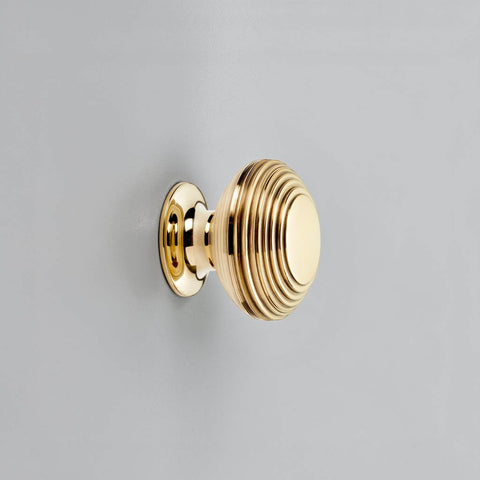 Aged brass beehive cupboard knob fitted on cabinet door, traditional reeded brass drawer knob close up