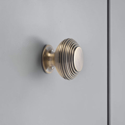 Large antique brass beehive cupboard knob fitted on cabinet door, traditional reeded brass drawer knob close up