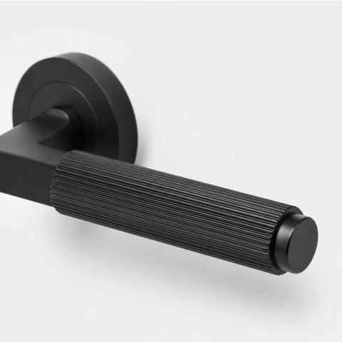 Close-up of black reeded lever door handle showing detailed linear grip texture and cylindrical end cap.