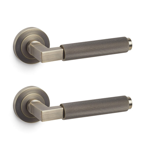 Pair of matt antique brass knurled lever door handles on round roses