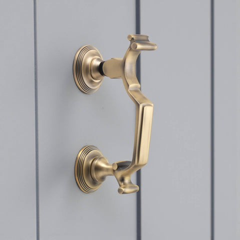 Matt antique brass reeded doctor door knocker mounted on grey door, angled side view showing circular backplates and brushed finish.