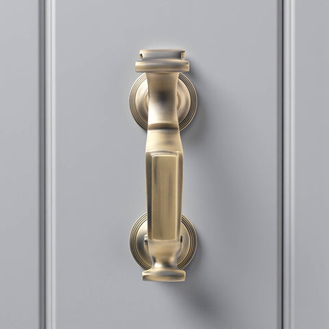 Front view of matt antique brass reeded doctor door knocker on grey door, displaying traditional doctor style design and soft aged brass finish.