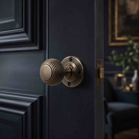 Matt antique brass sprung beehive mortice door knob fitted to a dark panelled interior door with matching antique brass tubular latch.