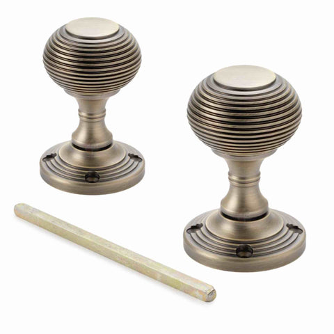Pair of matt antique brass sprung beehive mortice door knobs with matching spindle displayed on a white background.
