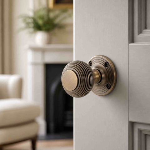 Matt antique brass sprung beehive mortice door knob fitted to a light grey panelled interior door in a traditional living room.