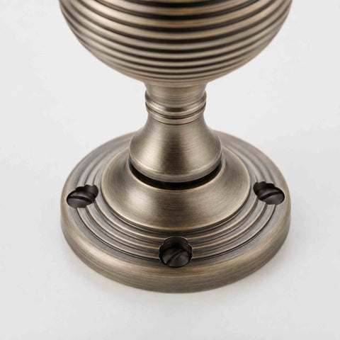 Close-up of matt antique brass beehive door knob backplate showing the reeded design and matching fixing screws.