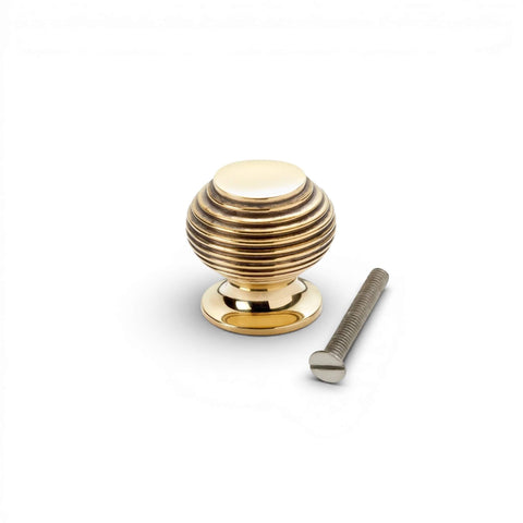 Small aged brass beehive cupboard knob with fixing screw, solid brass cabinet knob with reeded design on white background