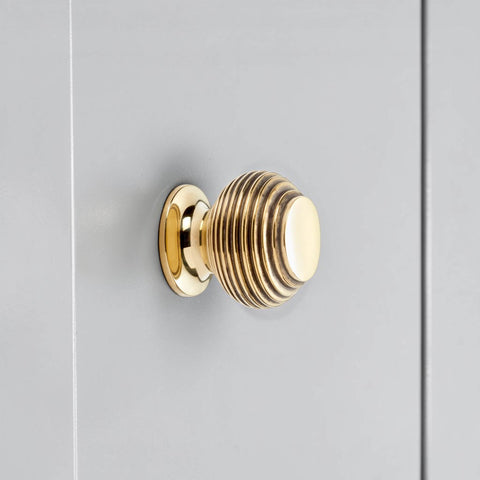 Small aged brass beehive cupboard knob fitted on cabinet door, traditional reeded brass drawer knob close up