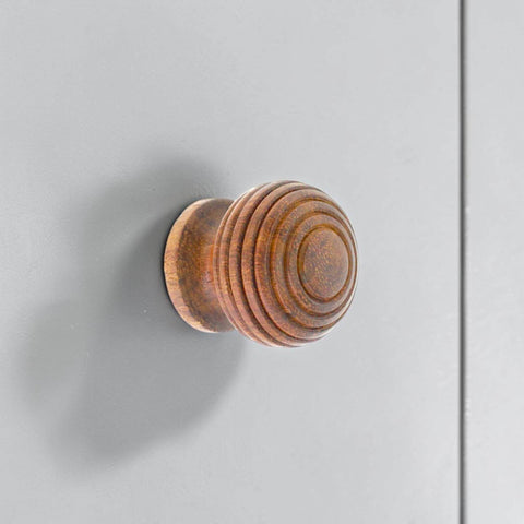 Small round rosewood beehive cupboard knob mounted on grey cabinet door