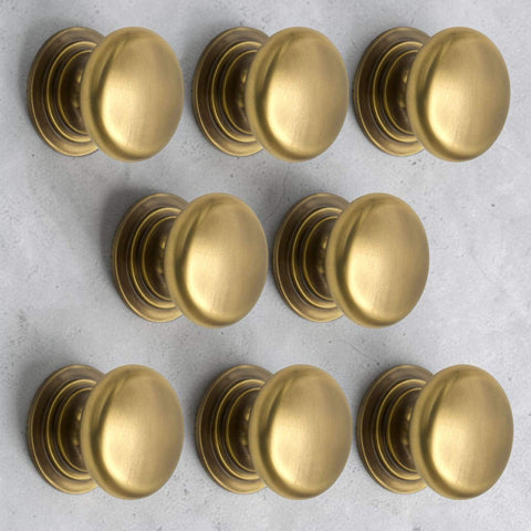Pack of 8 antique brass cupboard knobs on rose with smooth oval design and rear fixing M4 bolts supplied
