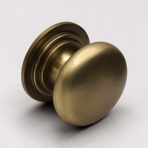 Side angle view of antique brass cupboard knob on rose with smooth oval face and stepped base