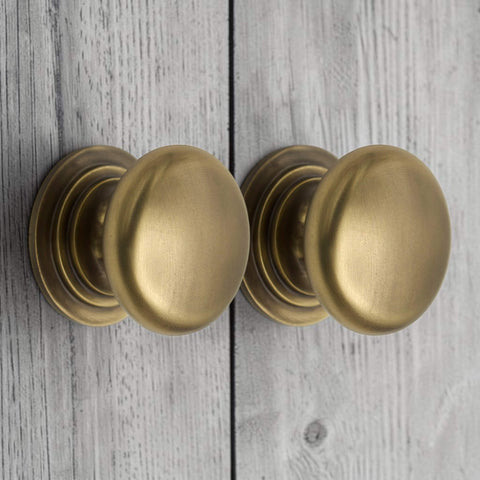 Pair of antique brass cupboard knobs fitted to cabinet doors with traditional stepped rose design