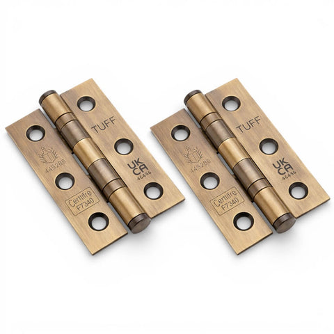 A pair of aged brass CE7 ball bearing butt hinges with fire-rated certification, shown at an angle on a white background