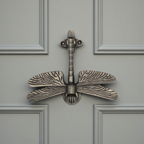 Pewter dragonfly door knocker mounted on a grey front door.