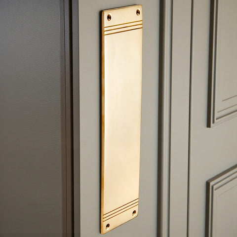 Unlacquered polished brass reeded push plate fitted to painted door, showing vertical installation and reflective finish